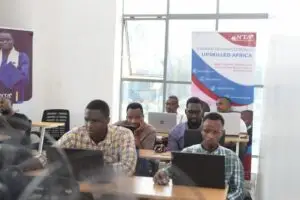 Grupo enfocado de profesionales africanos trabajando en laptops en un aula luminosa con pancartas educativas, incluyendo una que promueve el aumento de habilidades tecnológicas